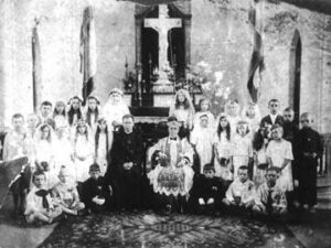 The photo donated by Zofia Brzezinska. Bishop Sliwowsky is seated next to an unknown priest. Zofia is the tall girl standing directly behind the bishop.